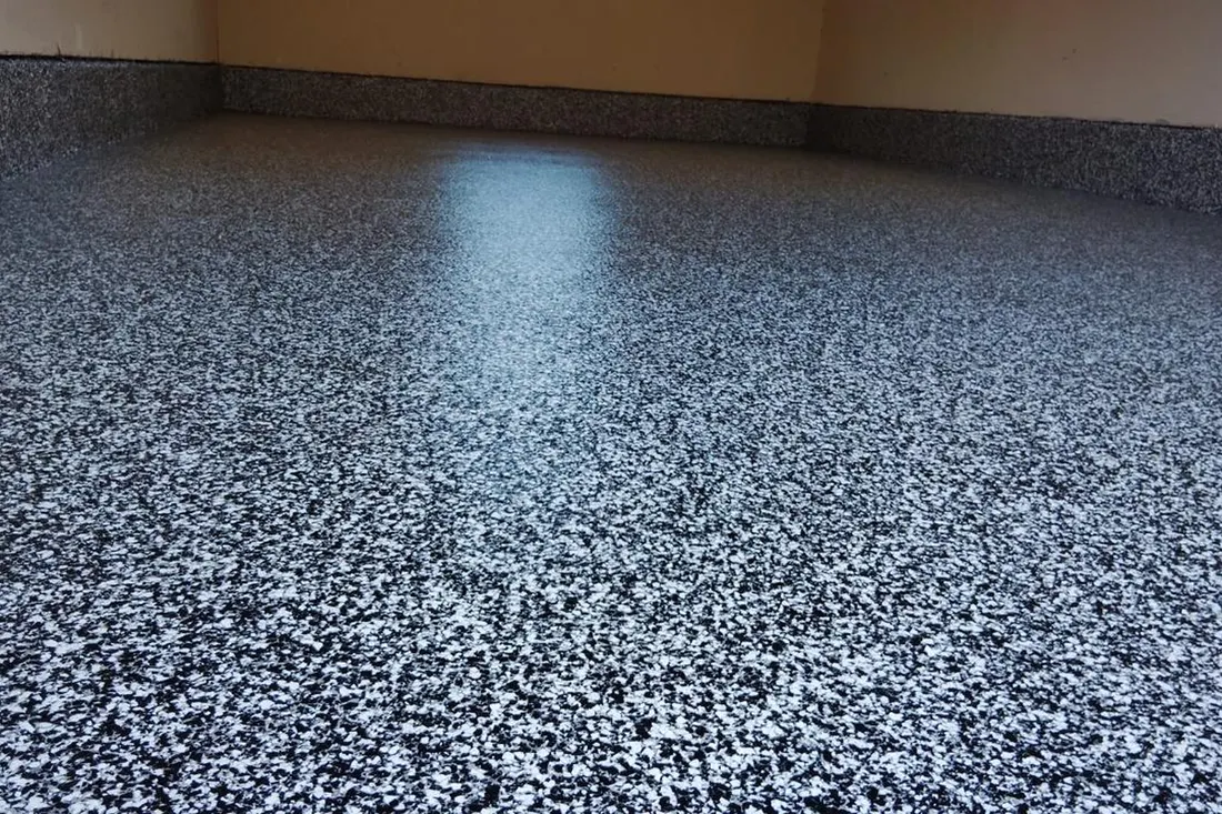 Glossy garage floor coated with speckled black, gray, and white epoxy flake finish extending up baseboards
