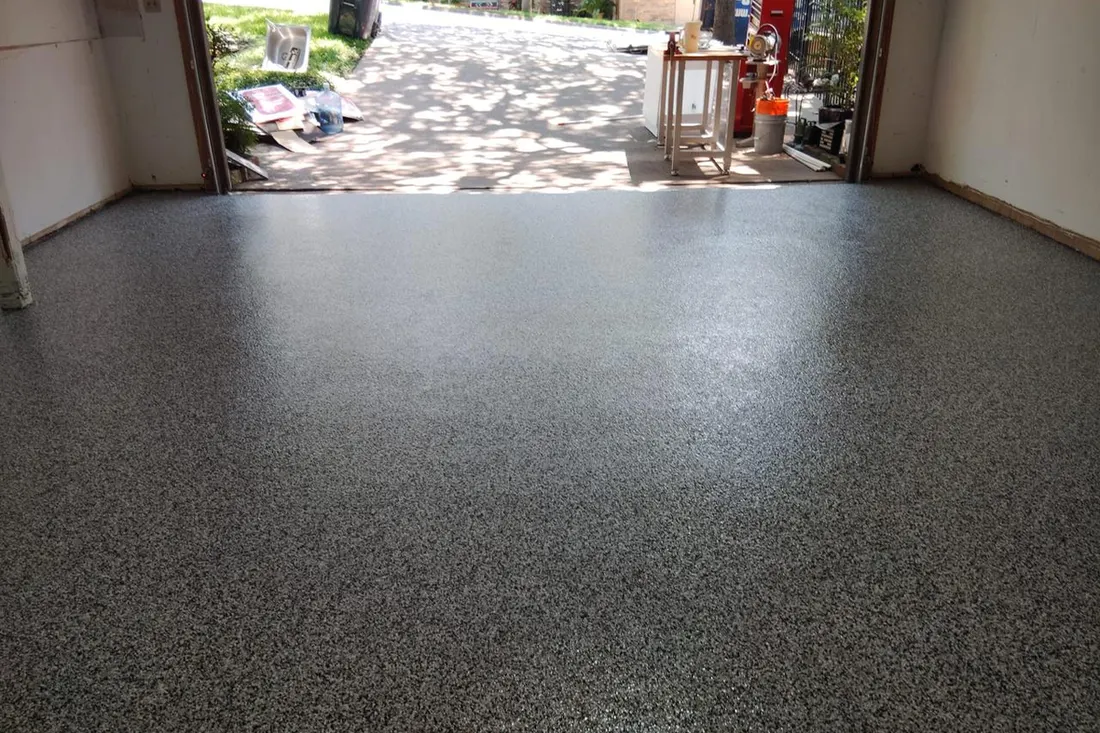 Glossy gray speckled epoxy coating on a residential garage floor leading to open doorway