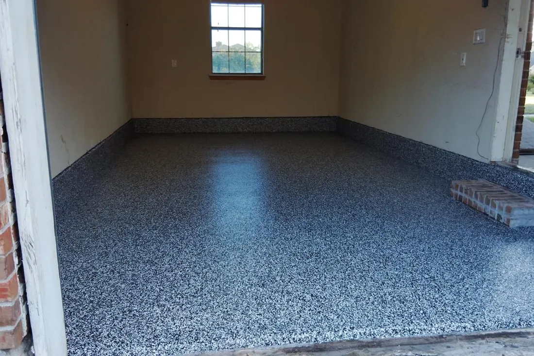 Empty garage interior featuring a glossy speckled gray epoxy floor coating extending up baseboards