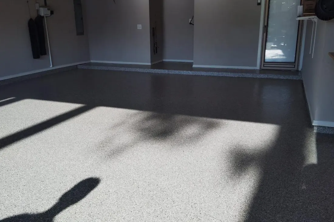 Freshly coated gray speckled epoxy garage floor illuminated by bright sunlight and soft shadows