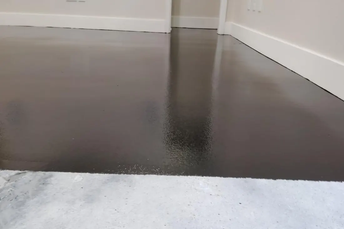 Glossy dark brown floor coating applied next to unfinished concrete along white baseboards and walls