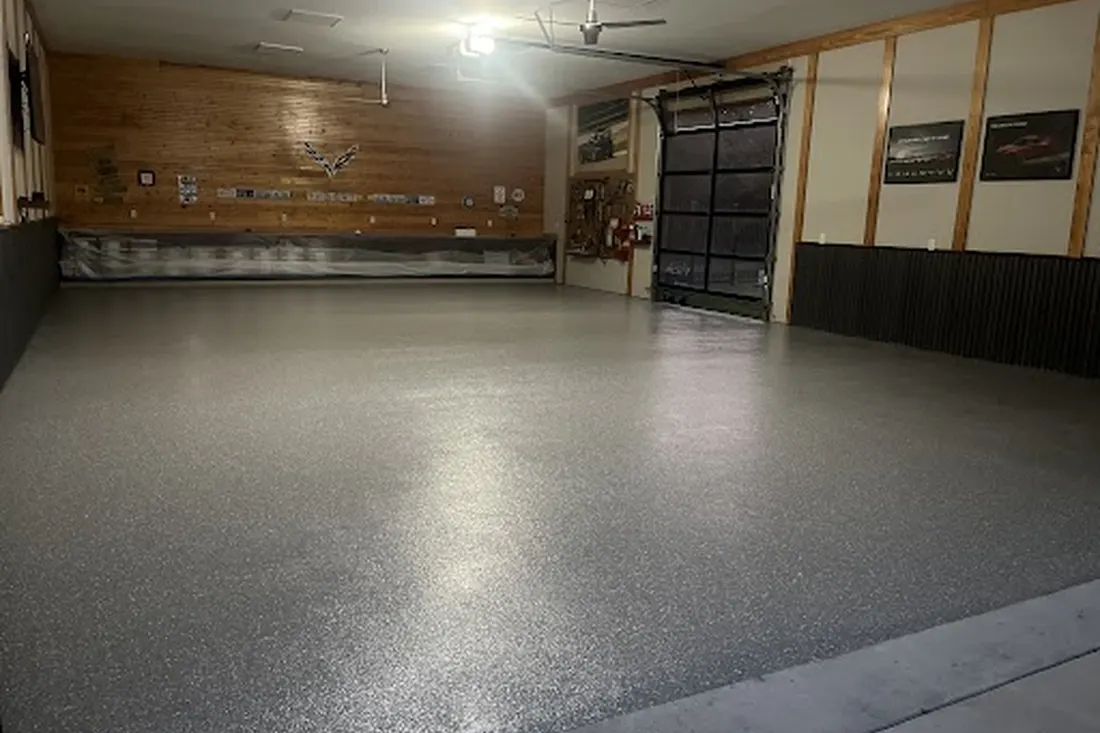 Spacious garage interior featuring glossy gray speckled coated concrete flooring and wood-paneled walls