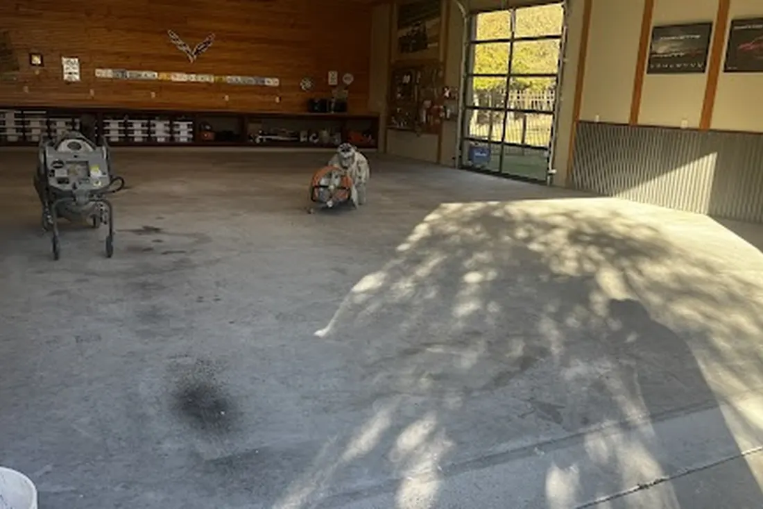 Unfinished concrete floor inside a garage workshop with floor grinding equipment and wooden walls