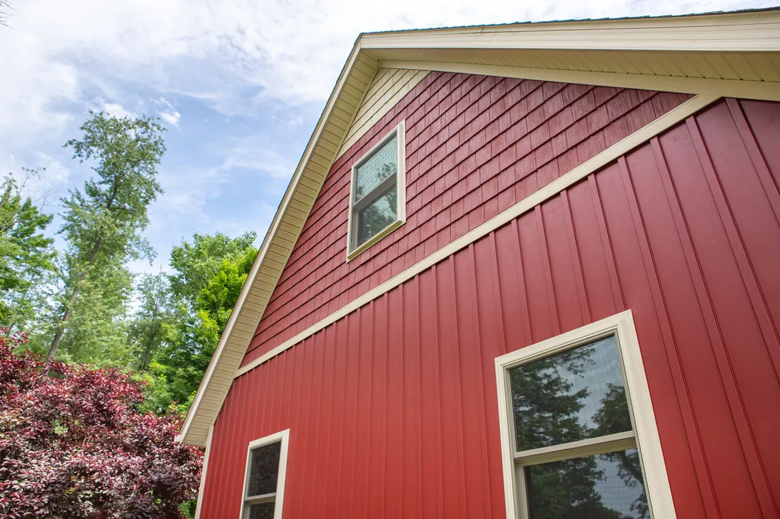 Red vertical siding and gable lap siding with cream trim on a house near trees
