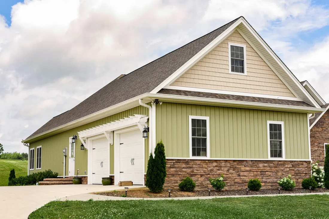 House featuring green vertical siding, stone veneer accents, and tan gable shakes beside a driveway