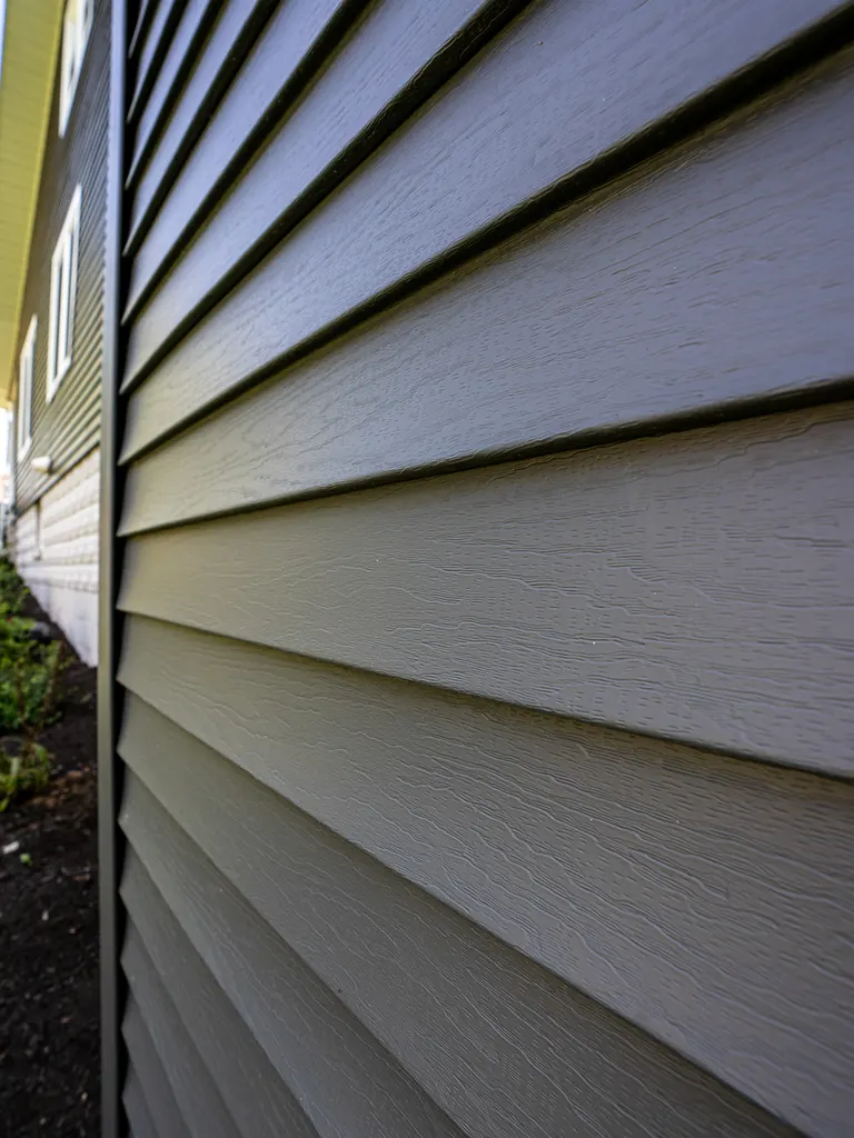 Close-up of dark gray wood-textured lap siding installed along an exterior house wall