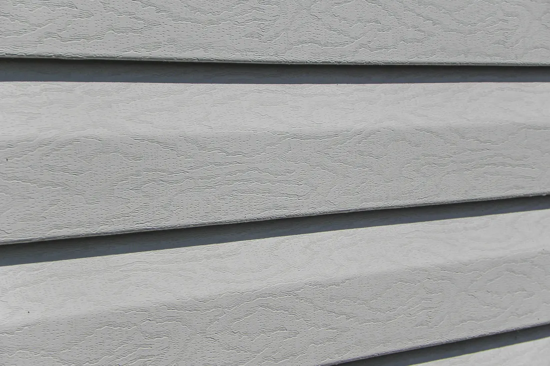 Close-up of light gray horizontal fiber cement lap siding with textured wood grain pattern