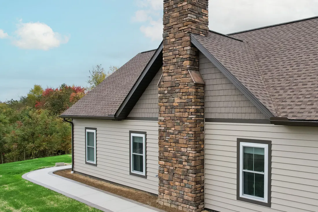 Beige horizontal siding and shake siding on a house exterior with stone chimney