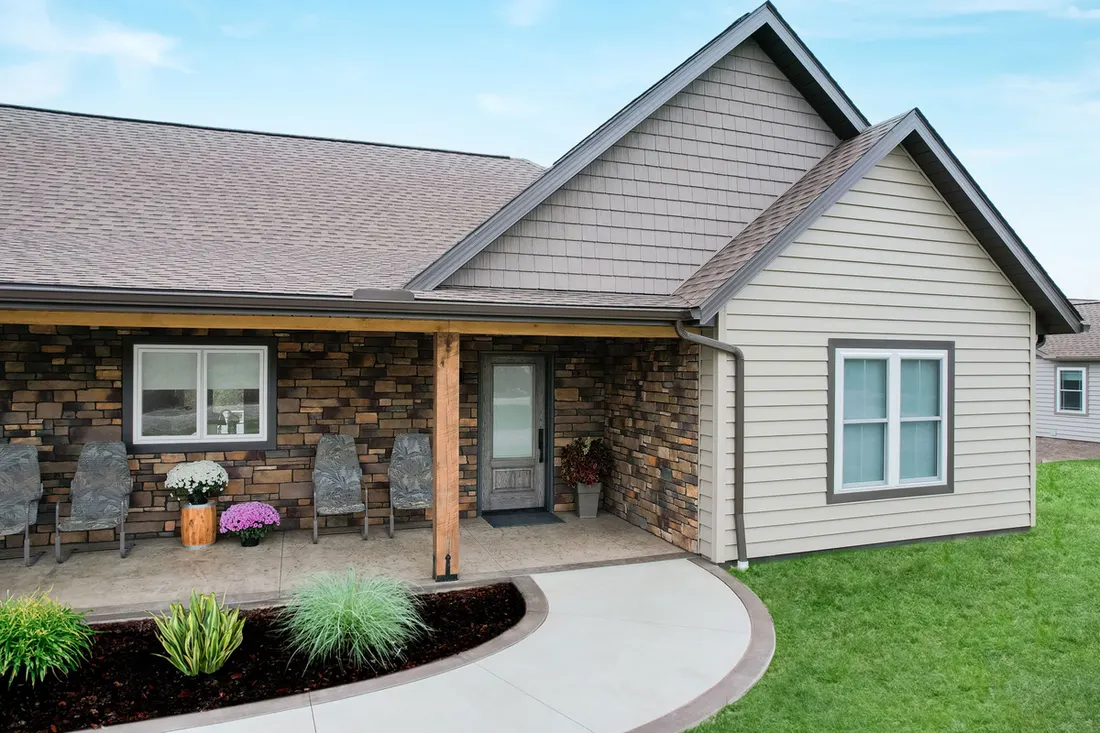 Home exterior featuring beige horizontal siding, gray shake gables, stacked stone veneer, and a covered porch