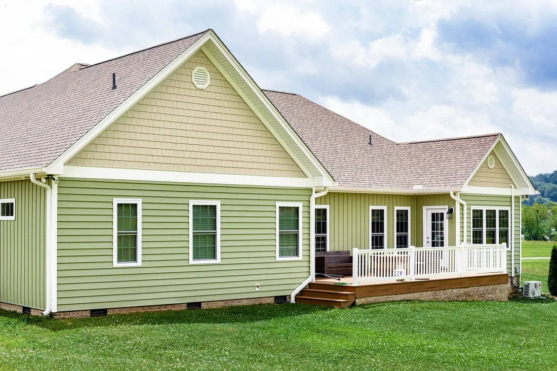 House exterior featuring light green horizontal siding, beige shingle gables, and a raised back deck