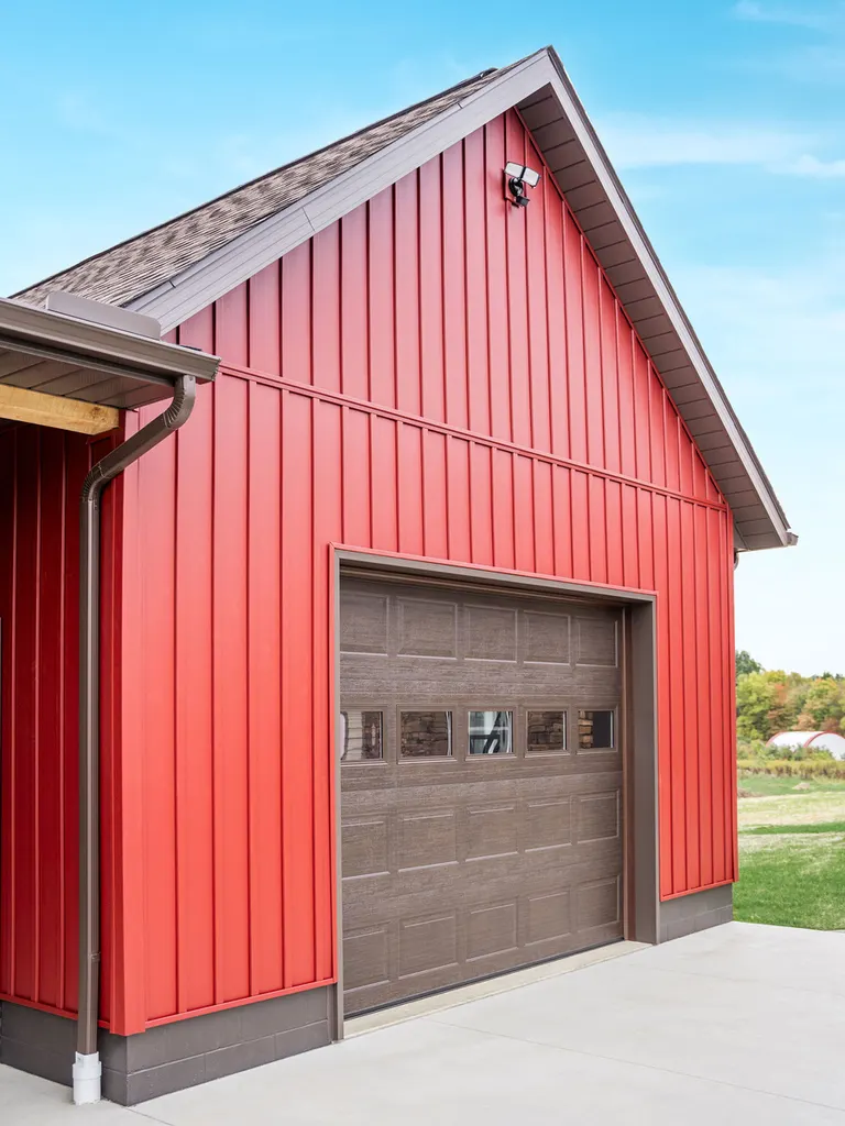 Red vertical insulated siding on a garage with a brown door and concrete driveway