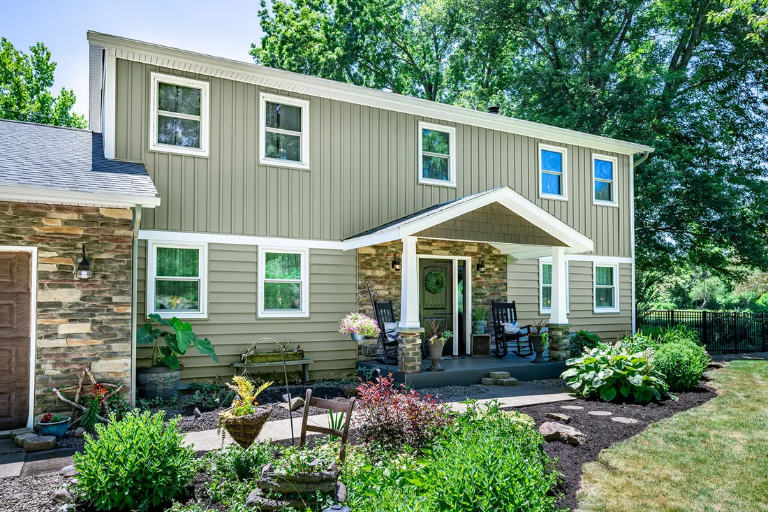 Two-story home with sage green vertical and horizontal siding, stone accents, and front porch