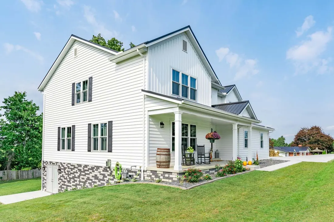 Two-story home with white insulated siding, black shutters, stone foundation, and a front porch