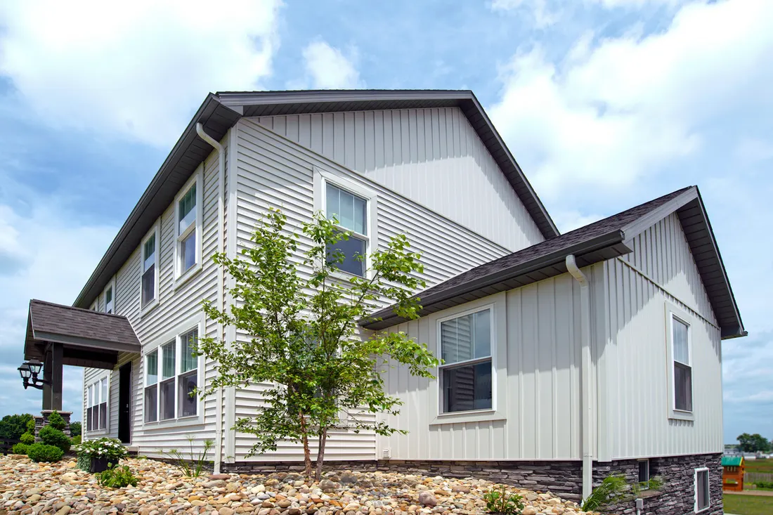 Two-story house with light vinyl siding, dark shingled roof, and stone veneer foundation accents