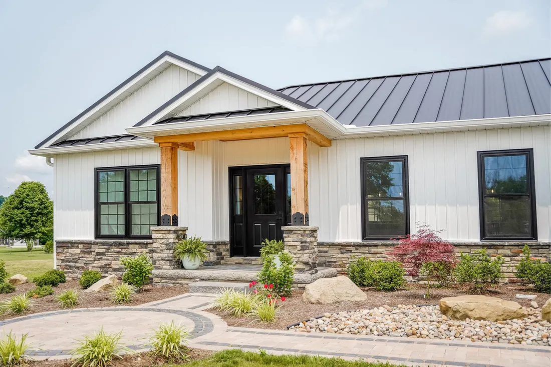 Modern home featuring white vertical siding, black metal roof, stone accents, and wood porch posts