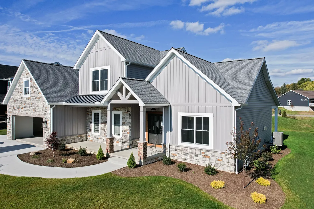Gray vinyl-sided house with white trim, stone accents, gabled rooflines, driveway, and landscaped lawn