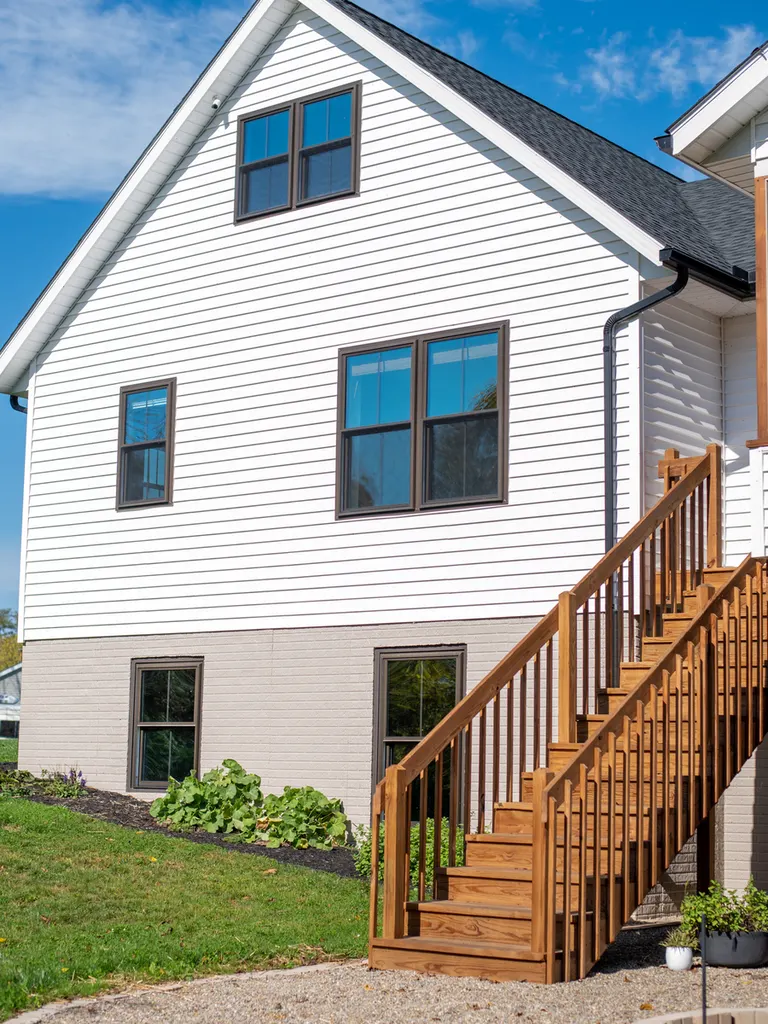 White horizontal vinyl siding on a two-story house with dark-trimmed windows and wooden exterior stairs