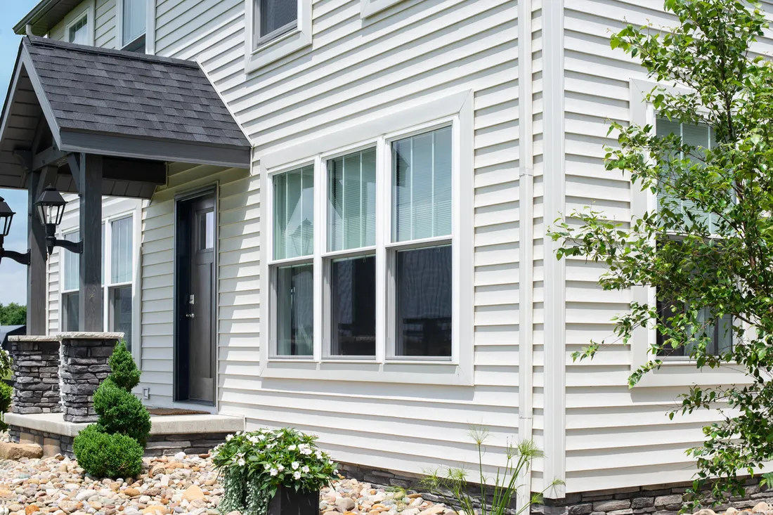 Two-story home exterior featuring white vinyl siding, large windows, and a dark front porch