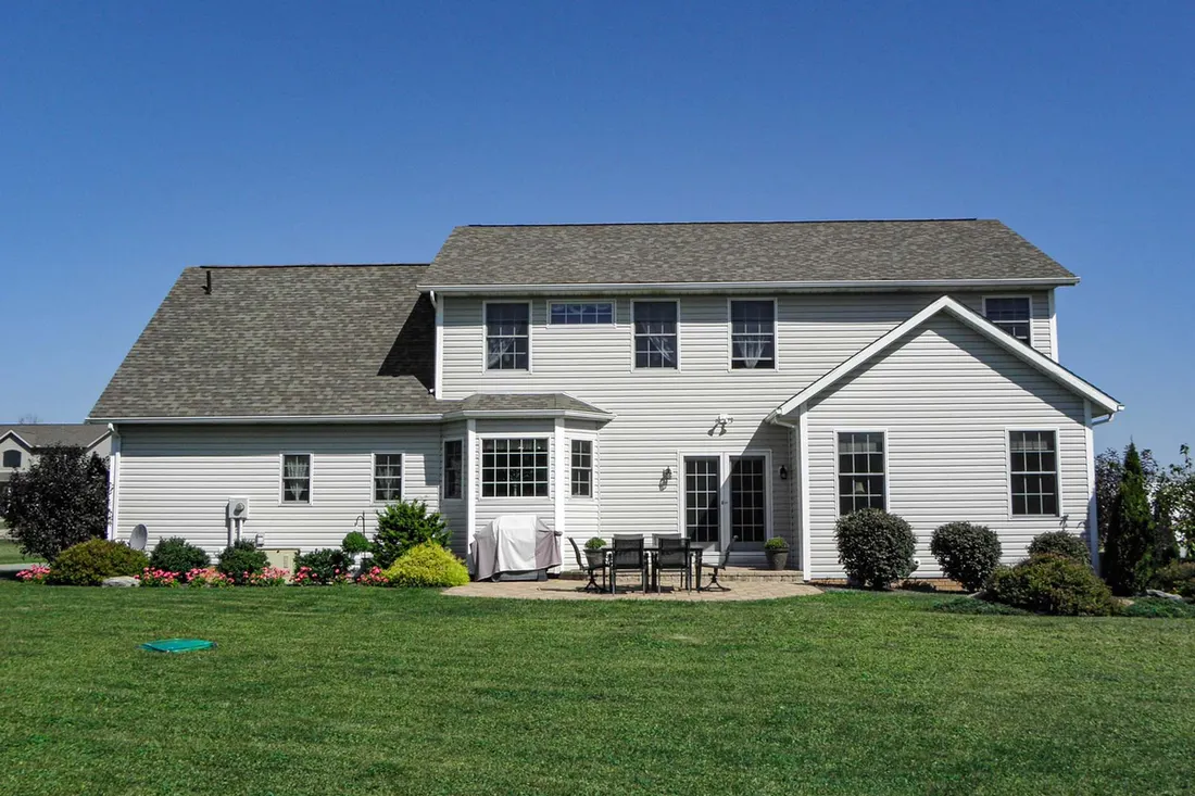 Rear exterior of a two-story house with light vinyl siding, patio, and lawn