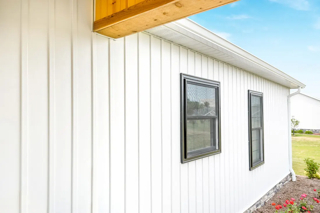 White vertical vinyl siding on a home exterior with black framed windows and wood trim
