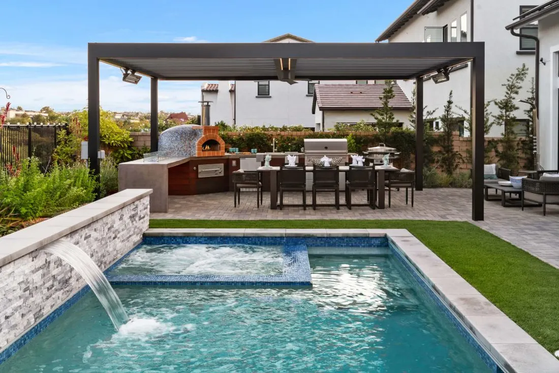 Pool and spa alongside a patio with black pergola, outdoor kitchen, and pizza oven
