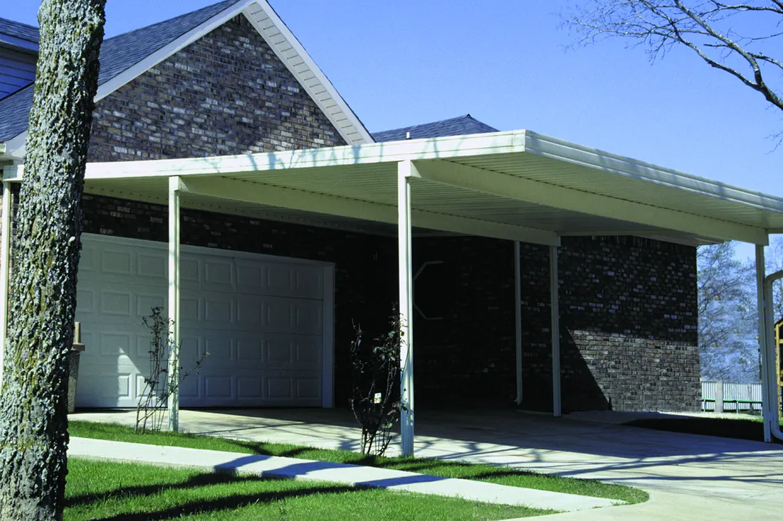 White metal carport structure installed over a concrete driveway beside a brick house
