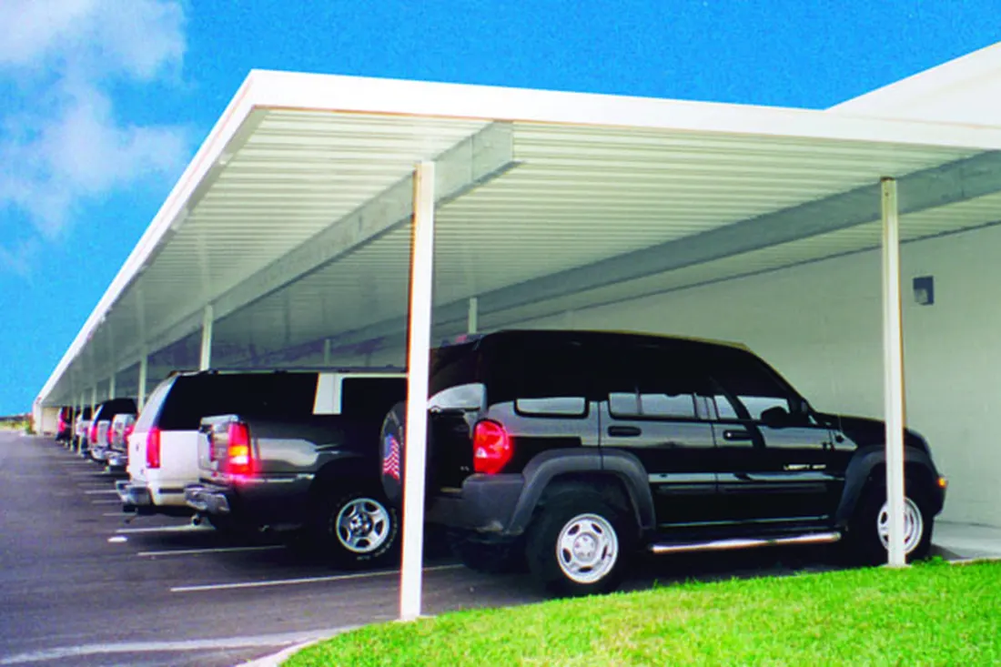 Long white metal carport covering a row of parked vehicles in an asphalt parking lot
