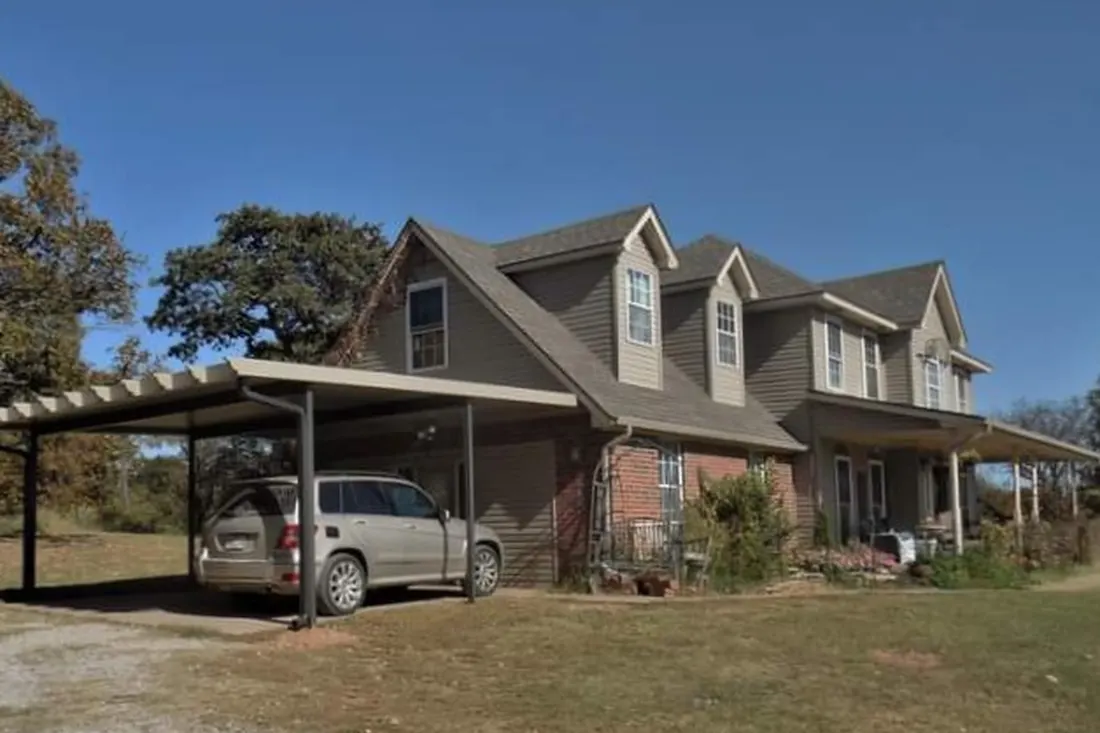 Metal attached carport covering a silver SUV beside a two-story residential house