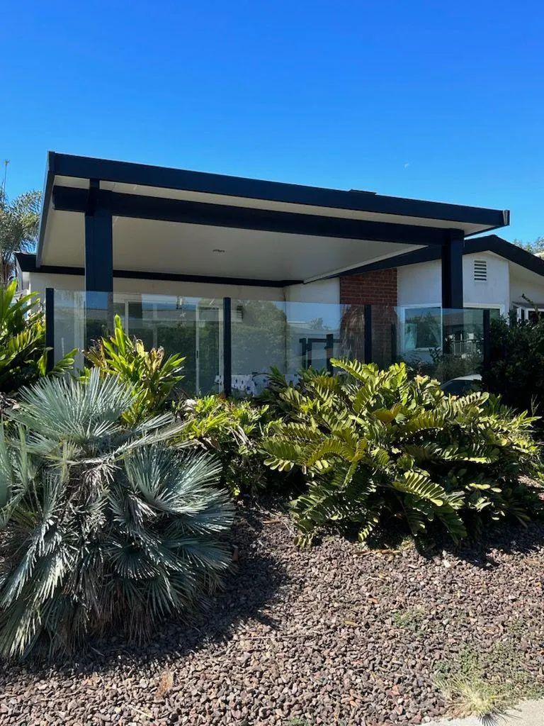 Modern black-framed patio cover with white ceiling, glass panels, and desert landscaping