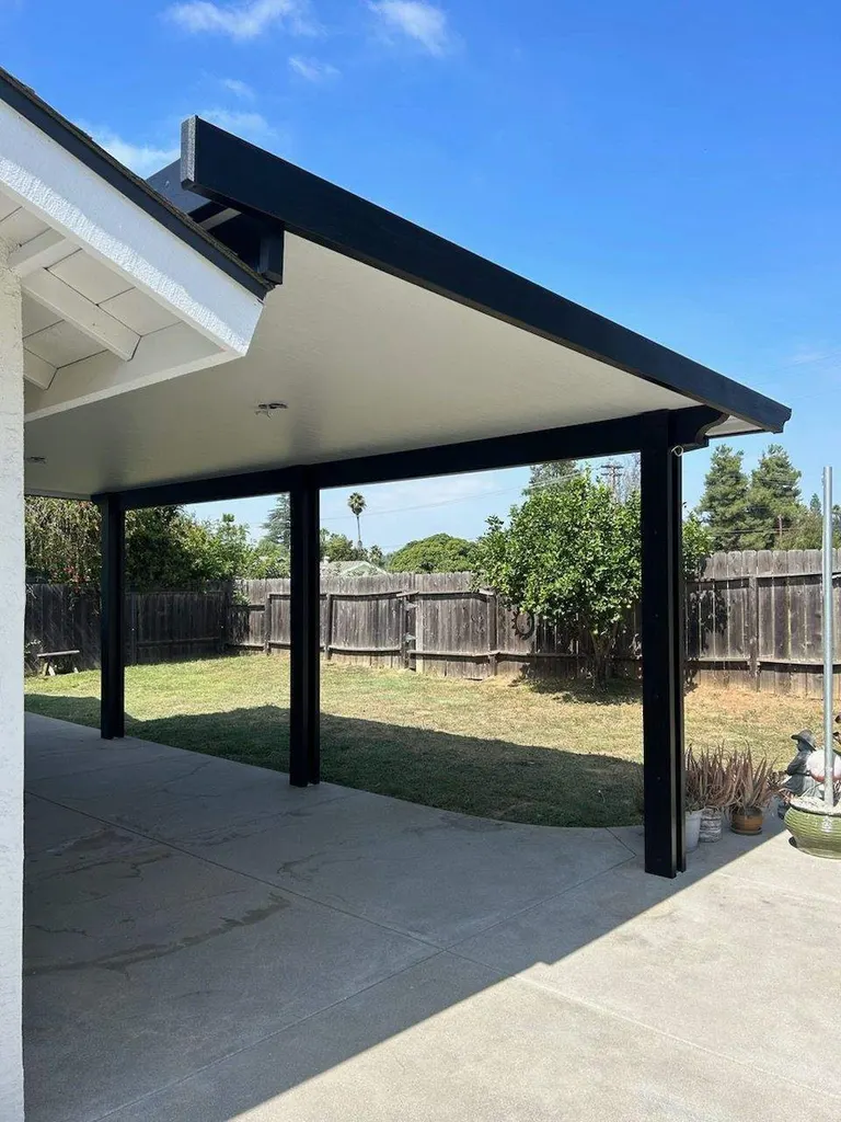 Black-framed patio cover with a white ceiling over a concrete patio and fenced backyard