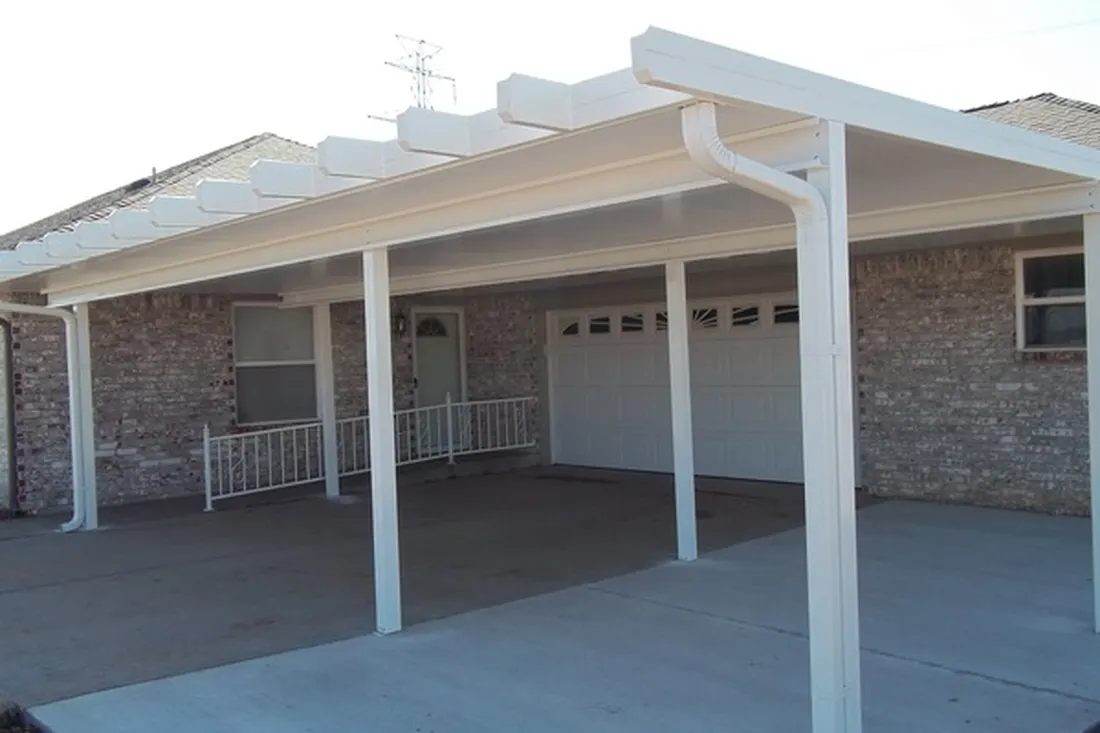 White patio cover with corrugated roof, supported by posts over a concrete driveway beside a brick home