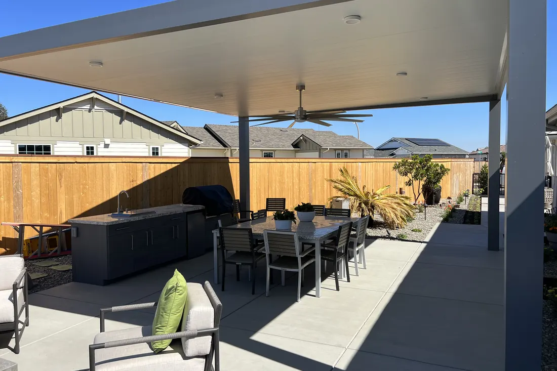 Covered patio with a flat roof, ceiling fan, gray posts, outdoor dining set, grill, and fenced yard