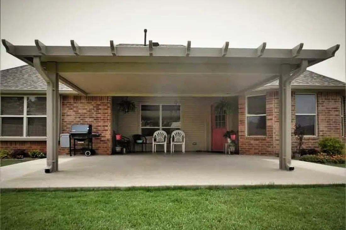 Neutral-toned solid patio cover with decorative pergola rafters over a concrete patio behind a brick house