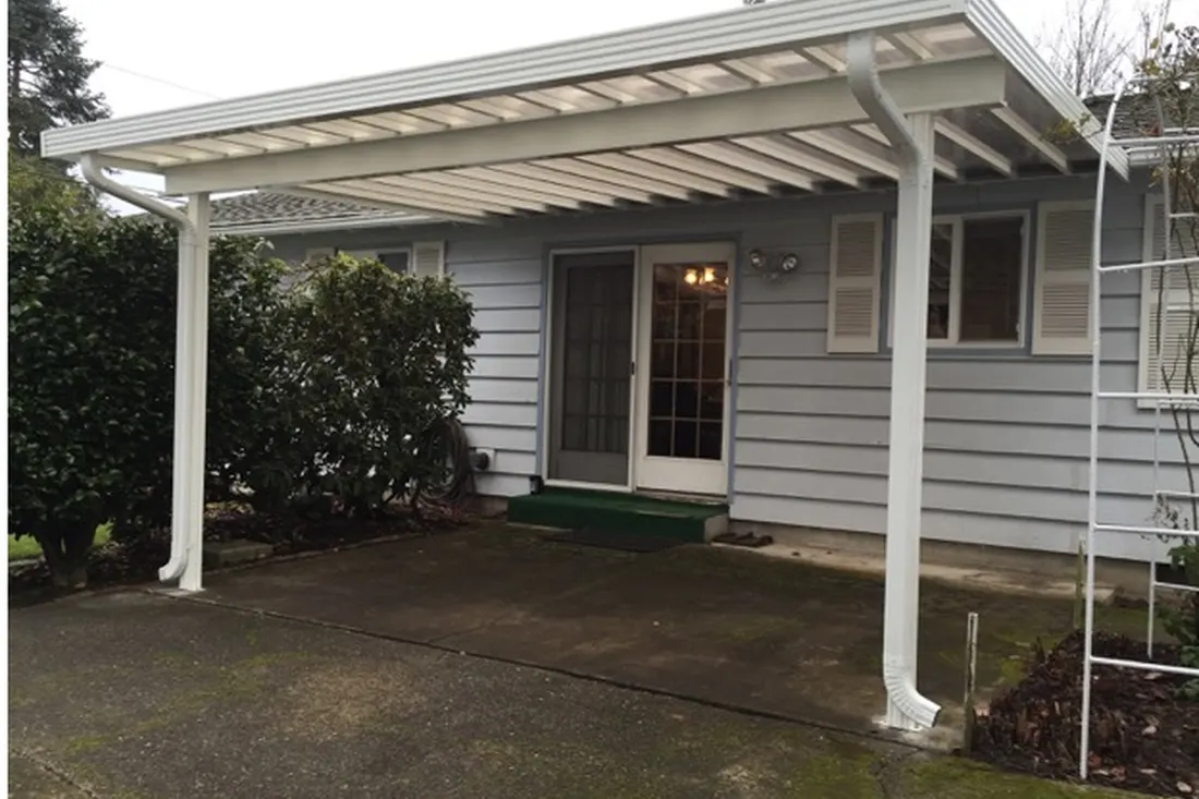 White patio cover with translucent roof panels beside a gray-sided house and concrete walkway