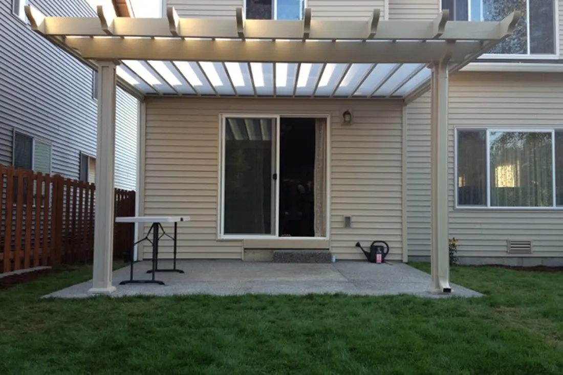 White patio cover with translucent roof panels beside a beige-sided house and small grassy yard