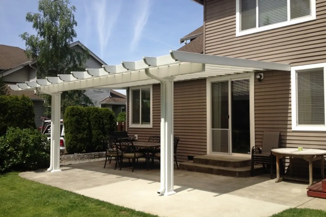 White solid patio cover attached to a brown vinyl-sided house over a stone terrace