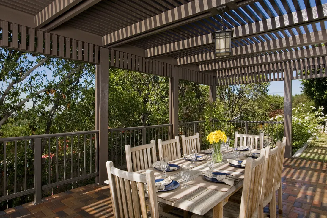 Wood patio cover with slatted roof, hanging lantern, dining table, and garden surroundings