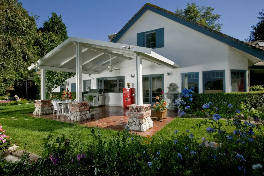White gabled patio cover with stone and brick columns over a backyard brick patio