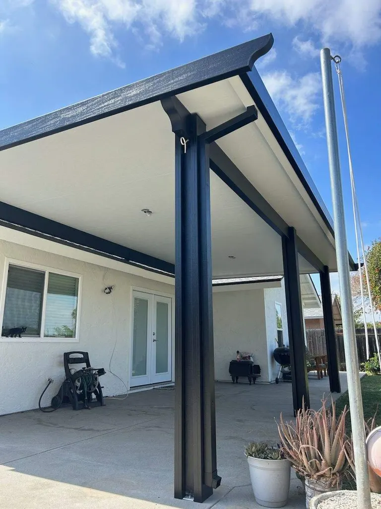 Patio cover attached to a house with black support posts over a concrete patio
