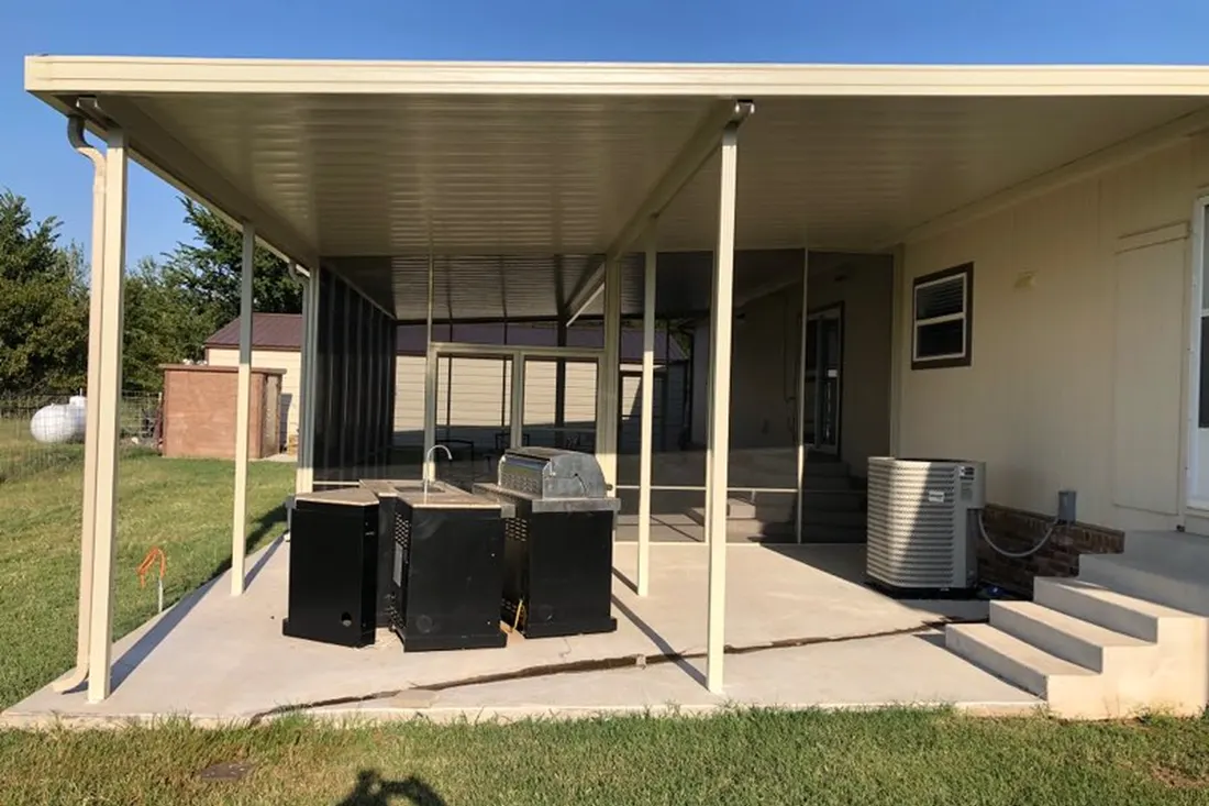 Covered patio with beige metal roof, slender posts, concrete slab, outdoor equipment, steps, and grassy yard