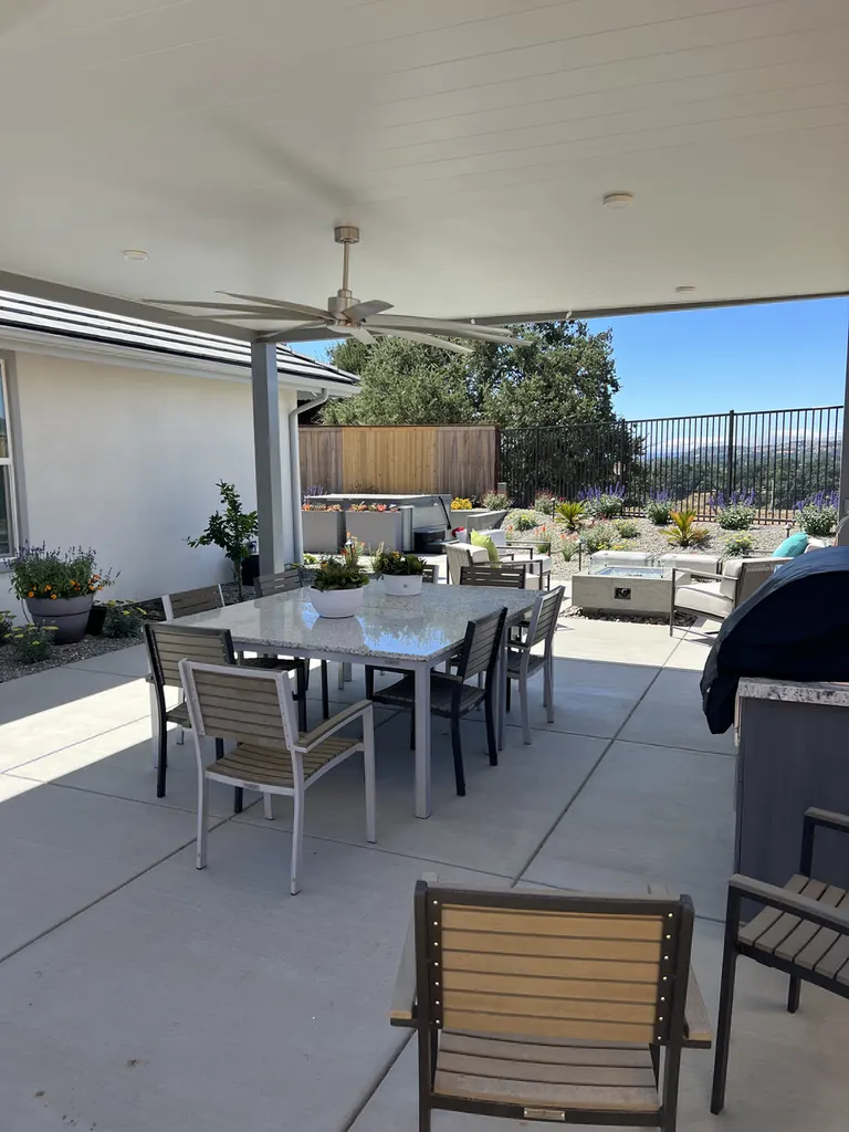 Covered patio with white ceiling, ceiling fan, gray columns, dining set, outdoor kitchen, and garden views