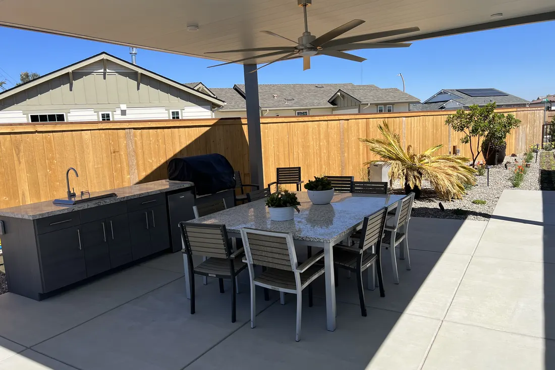 Solid patio cover with ceiling fan over backyard dining area, outdoor kitchen, and concrete patio