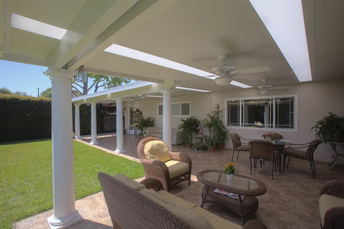 White solid patio cover with skylights and round columns sheltering an outdoor wicker seating area