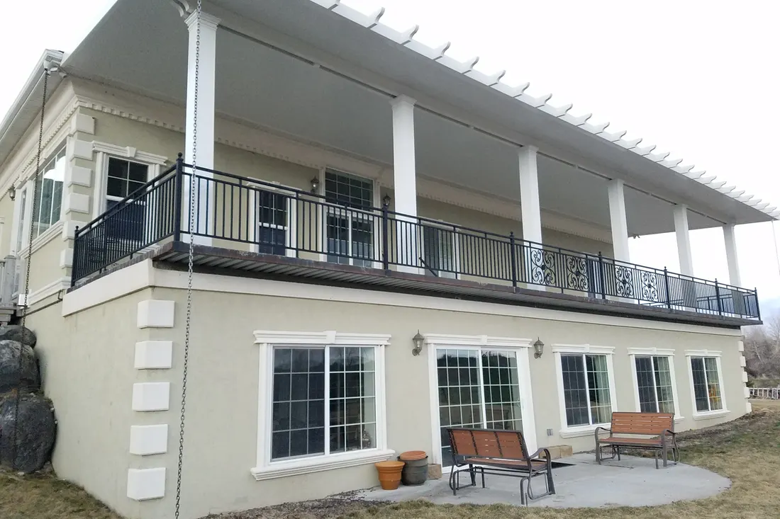 White patio cover with support columns over an elevated deck on a two-story beige house