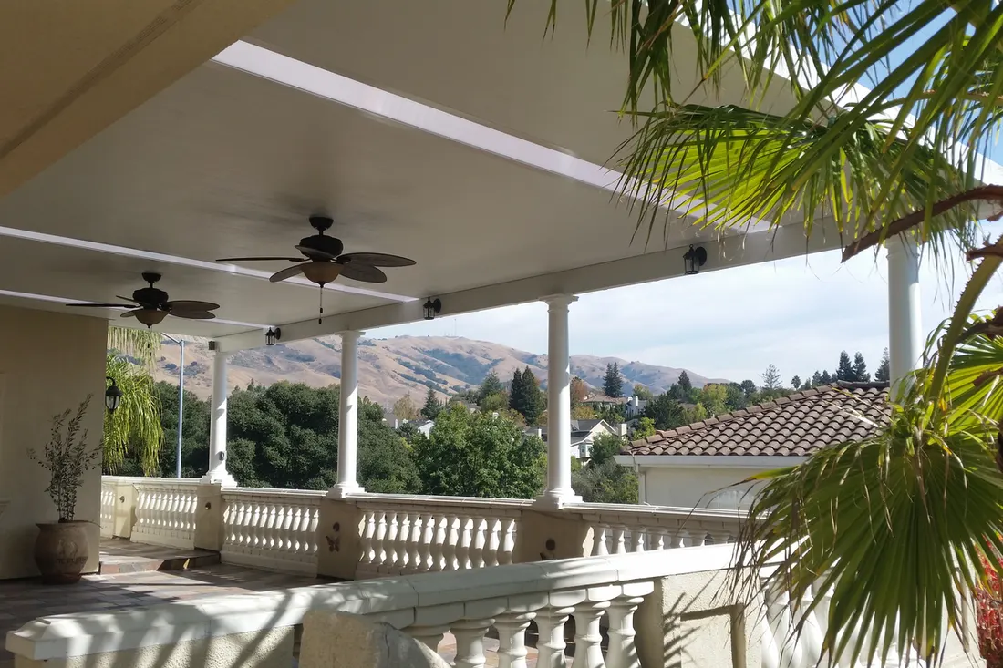 White solid patio cover with ceiling fans and columns over a balcony overlooking distant hills