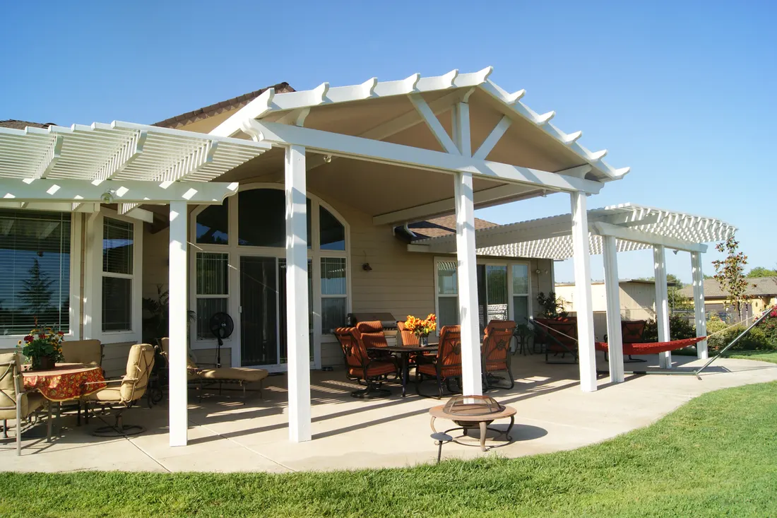 White patio cover with slatted pergola extensions, outdoor seating, concrete patio, and surrounding lawn