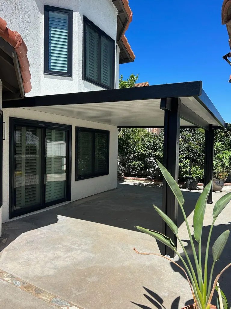 Black aluminum patio cover with white ceiling panels attached to a home over concrete