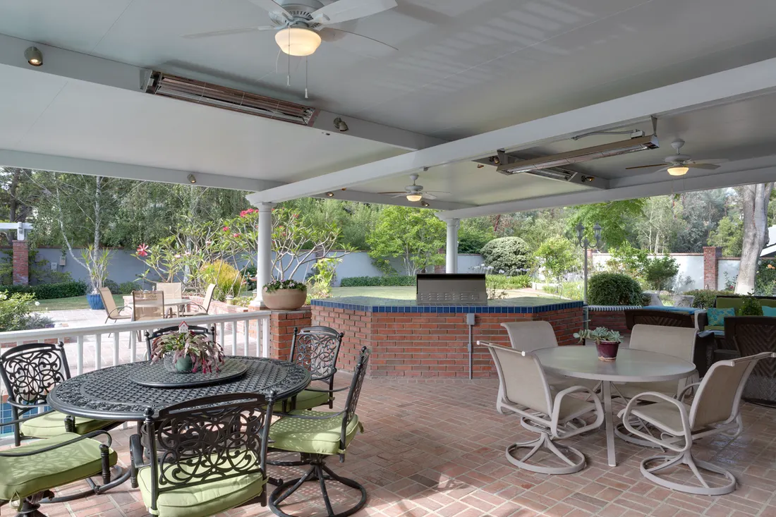 White solid patio cover with heaters and ceiling fans over a brick outdoor dining area