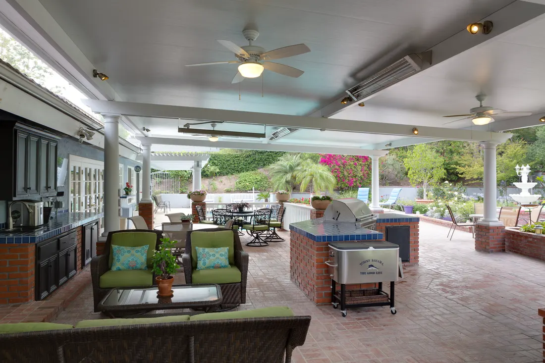 Covered patio with white beams, brick flooring, outdoor kitchen, ceiling fans, and garden views