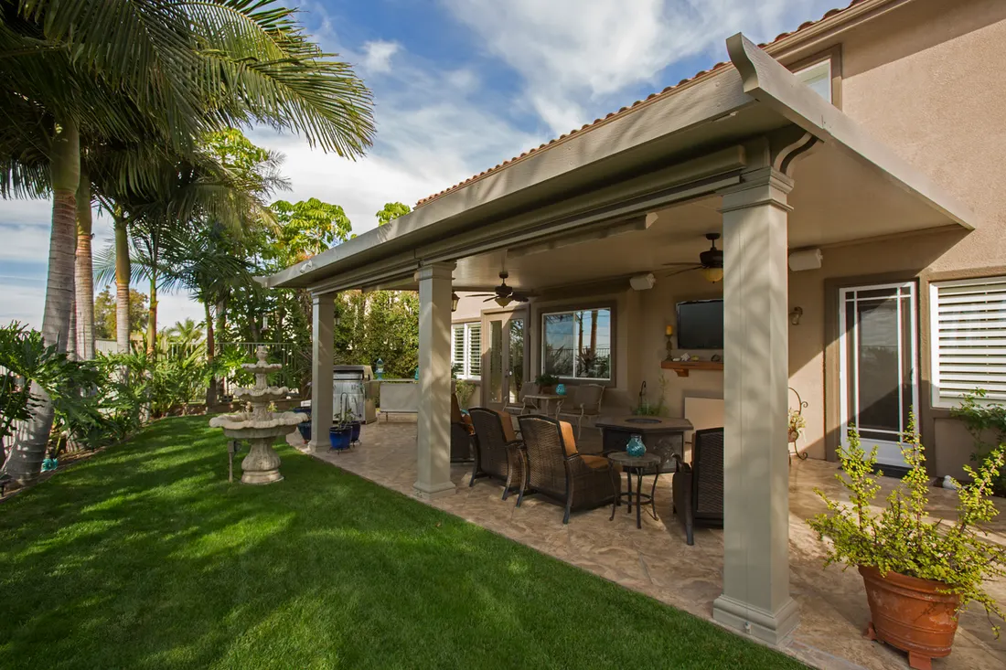 Solid beige patio cover with square columns over a furnished stone backyard patio